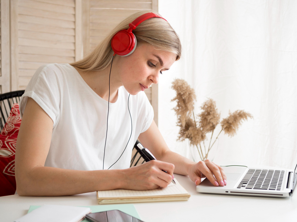 Chica concentrada estudiando con audífonos, usando música para mejorar su concentración.